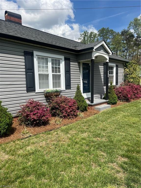 view of exterior entry with a lawn and a chimney