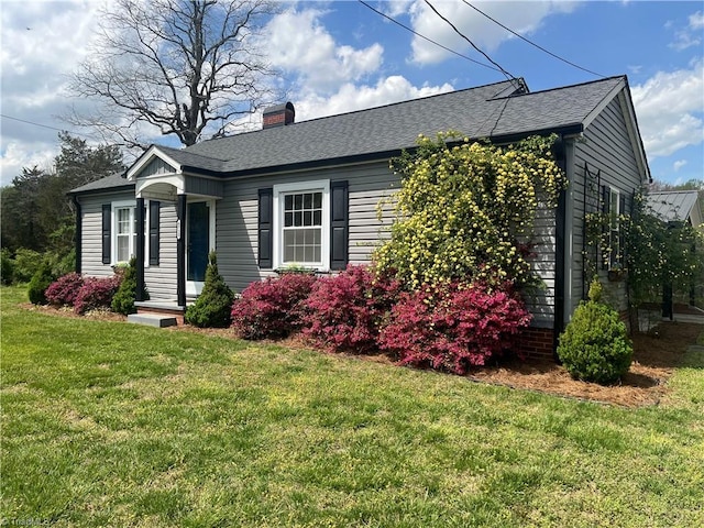 view of front facade with a front lawn, a shingled roof, and a chimney