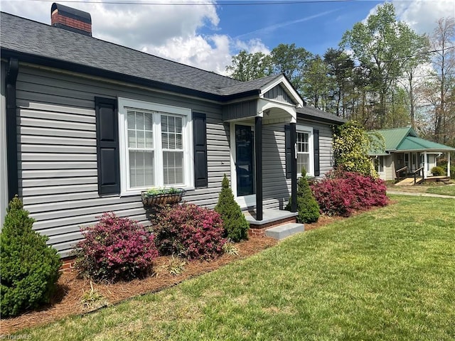 exterior space with a yard, a shingled roof, and a chimney