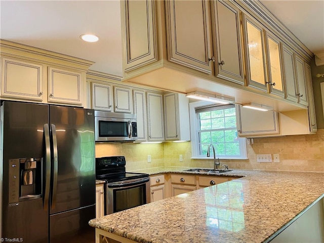 kitchen featuring cream cabinets, appliances with stainless steel finishes, backsplash, a sink, and a peninsula