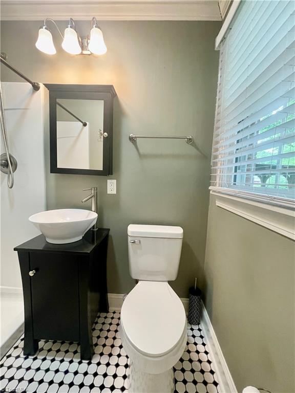 bathroom with ornamental molding, toilet, vanity, baseboards, and a shower