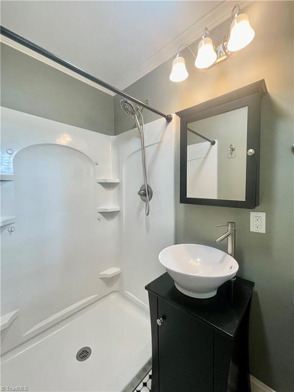 bathroom featuring walk in shower, crown molding, and vanity
