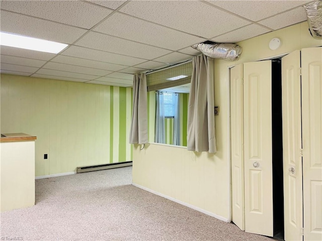 below grade area featuring a paneled ceiling, carpet flooring, baseboards, and a baseboard radiator