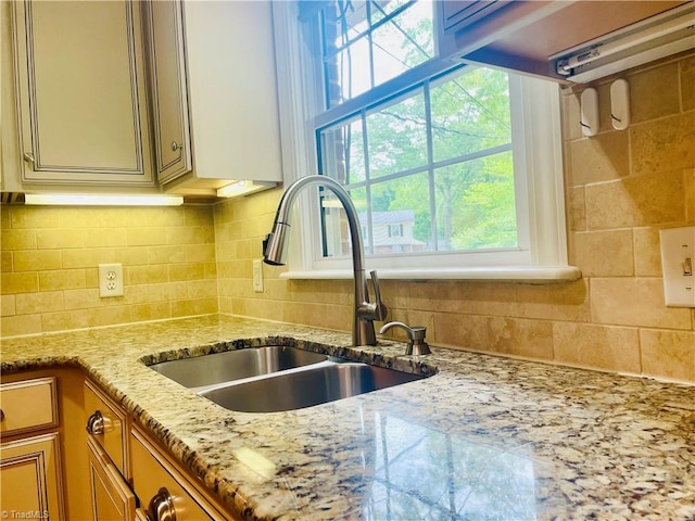details with decorative backsplash, light stone countertops, brown cabinetry, and a sink