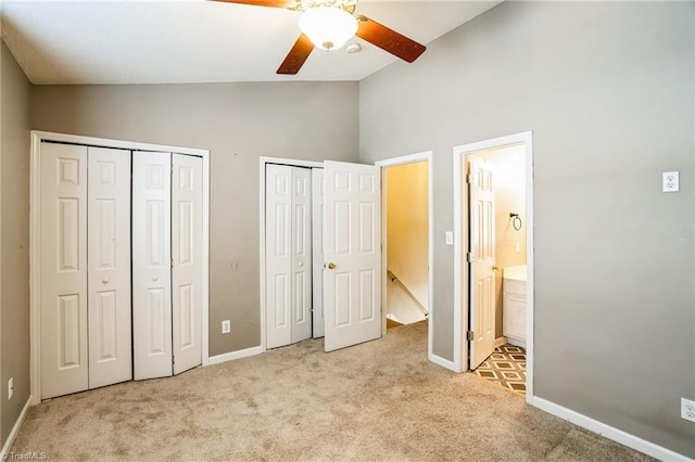 unfurnished bedroom with ceiling fan, ensuite bathroom, light carpet, vaulted ceiling, and multiple closets