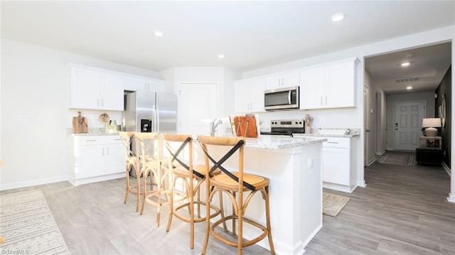 kitchen with white cabinets, stainless steel appliances, light hardwood / wood-style flooring, and a kitchen island with sink