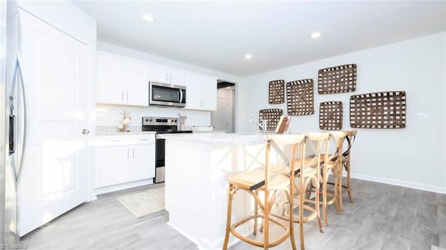 kitchen with appliances with stainless steel finishes, a kitchen breakfast bar, a center island with sink, white cabinets, and light hardwood / wood-style floors