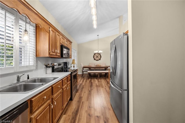 kitchen with hanging light fixtures, sink, stainless steel appliances, light wood-type flooring, and vaulted ceiling