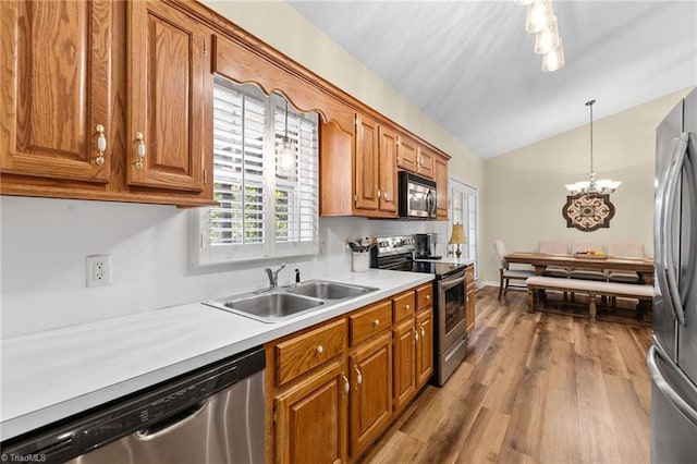 kitchen featuring appliances with stainless steel finishes, pendant lighting, lofted ceiling, hardwood / wood-style flooring, and sink