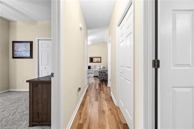 hallway with a textured ceiling, light wood-type flooring, and vaulted ceiling