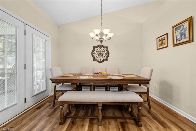 dining area with a notable chandelier, wood-type flooring, and vaulted ceiling