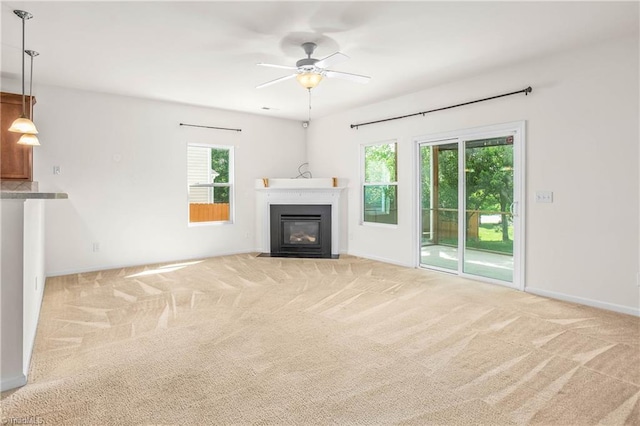 unfurnished living room featuring a ceiling fan, a fireplace with flush hearth, light colored carpet, and baseboards
