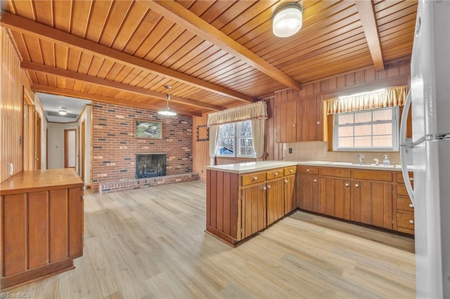 kitchen featuring brown cabinets, a fireplace, freestanding refrigerator, beamed ceiling, and a peninsula