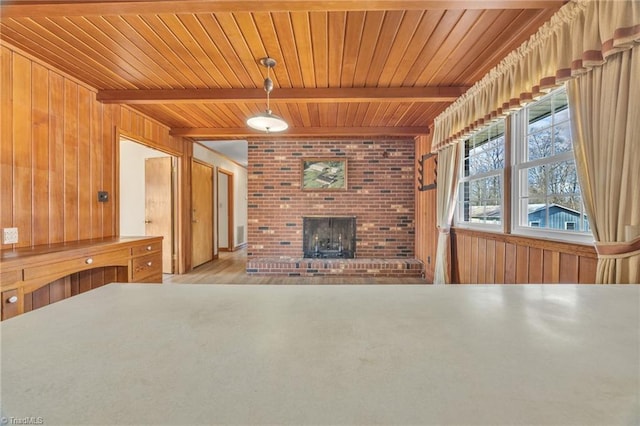 unfurnished living room featuring a brick fireplace, wooden ceiling, wooden walls, and beam ceiling