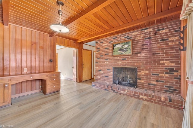 unfurnished living room featuring built in study area, wood ceiling, wood finished floors, beamed ceiling, and a brick fireplace