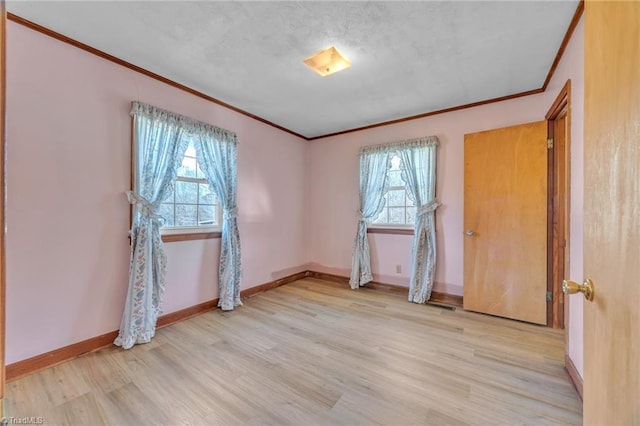 spare room featuring light wood finished floors, baseboards, and crown molding