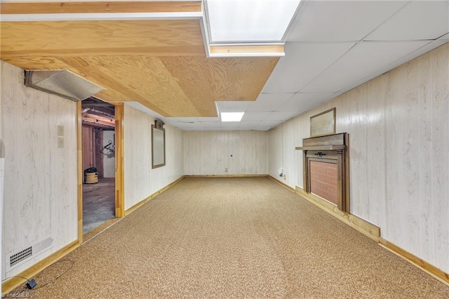 finished basement featuring light colored carpet, a paneled ceiling, visible vents, and wooden walls