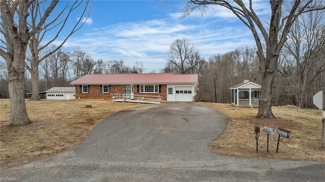 single story home with aphalt driveway, brick siding, covered porch, metal roof, and a garage