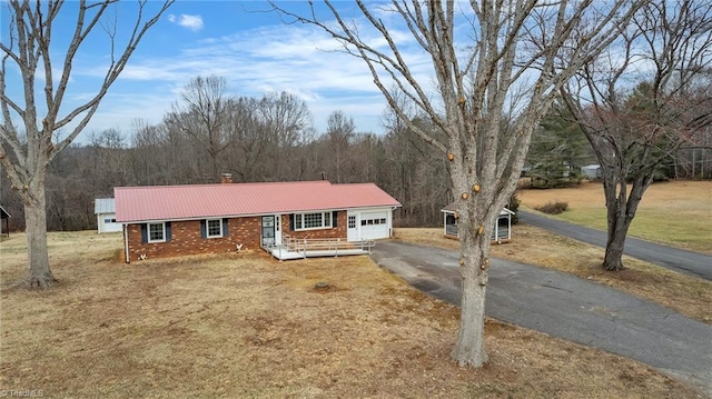 ranch-style house featuring driveway, a view of trees, metal roof, an attached garage, and brick siding