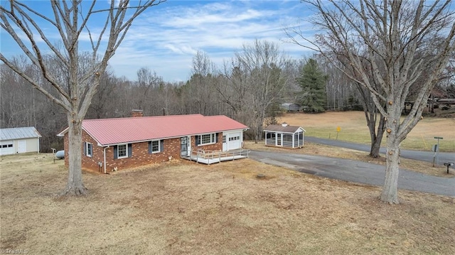 ranch-style home featuring brick siding, a chimney, metal roof, a garage, and driveway