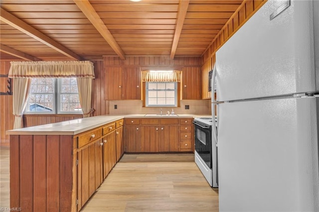 kitchen featuring electric stove, brown cabinets, light countertops, freestanding refrigerator, and a peninsula