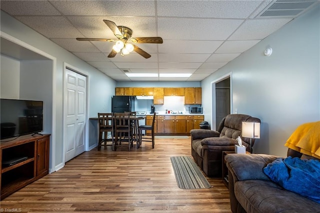 living area with wood finished floors, visible vents, a drop ceiling, and ceiling fan