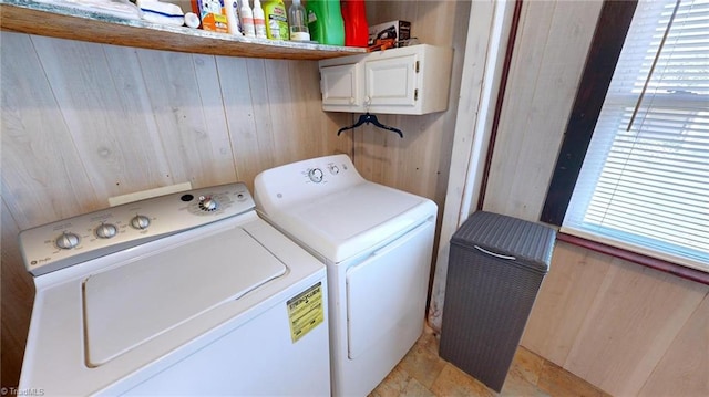 laundry area featuring separate washer and dryer, cabinets, and wood walls