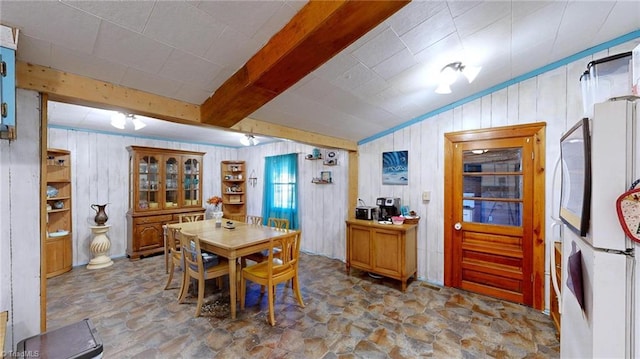 dining space with wooden walls and beamed ceiling