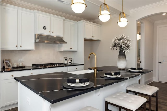 kitchen with under cabinet range hood, decorative backsplash, dark countertops, and ornamental molding