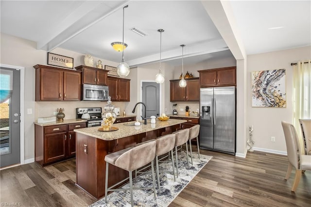 kitchen with appliances with stainless steel finishes, a kitchen island with sink, sink, pendant lighting, and beamed ceiling