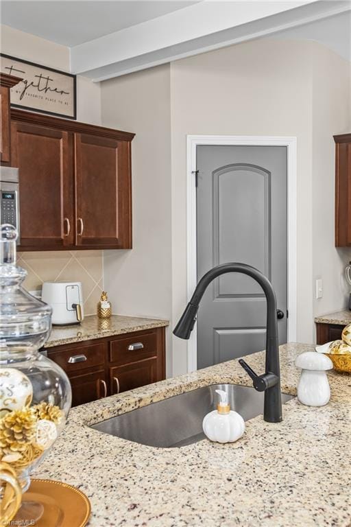 kitchen featuring decorative backsplash, sink, and light stone counters