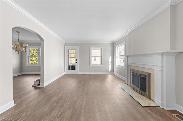 unfurnished living room featuring a tile fireplace, an inviting chandelier, ornamental molding, and plenty of natural light