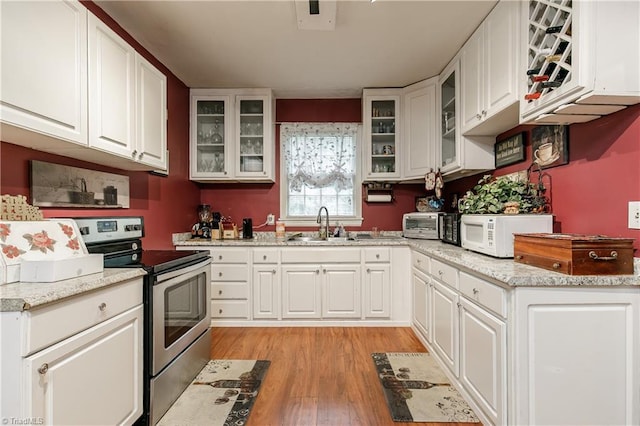 kitchen featuring light stone counters, white cabinets, stainless steel range with electric stovetop, and light wood-type flooring