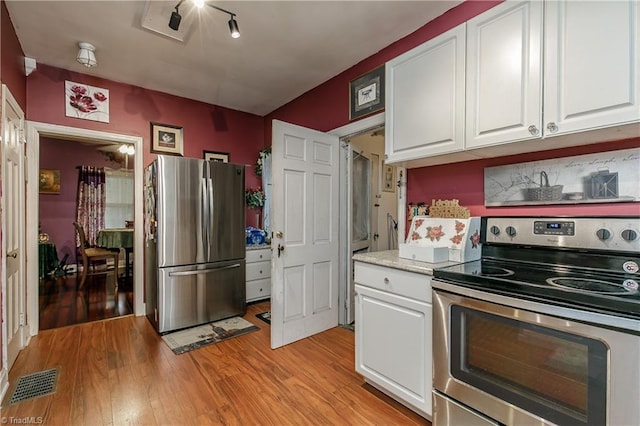 kitchen with white cabinets, light wood-type flooring, and appliances with stainless steel finishes