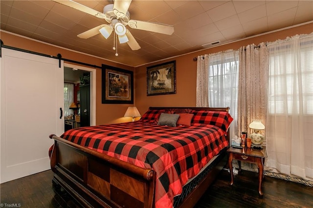 bedroom featuring dark hardwood / wood-style flooring, a barn door, ceiling fan, and ornamental molding