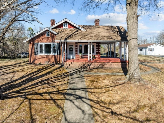 view of front of home with brick siding, a chimney, and a porch