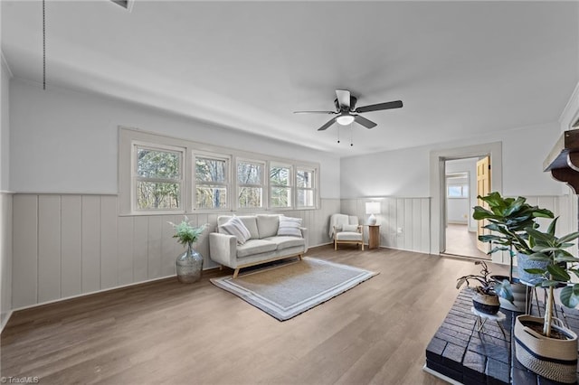 living room with a ceiling fan, a wealth of natural light, a wainscoted wall, and wood finished floors