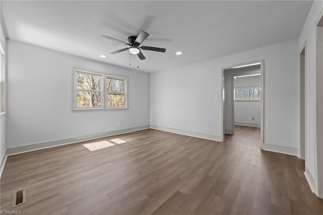 empty room featuring a wealth of natural light, wood finished floors, visible vents, and baseboards