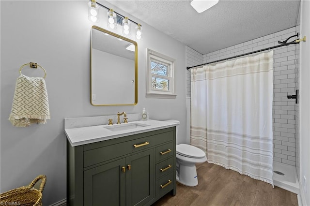 full bath with toilet, wood finished floors, a tile shower, a textured ceiling, and vanity