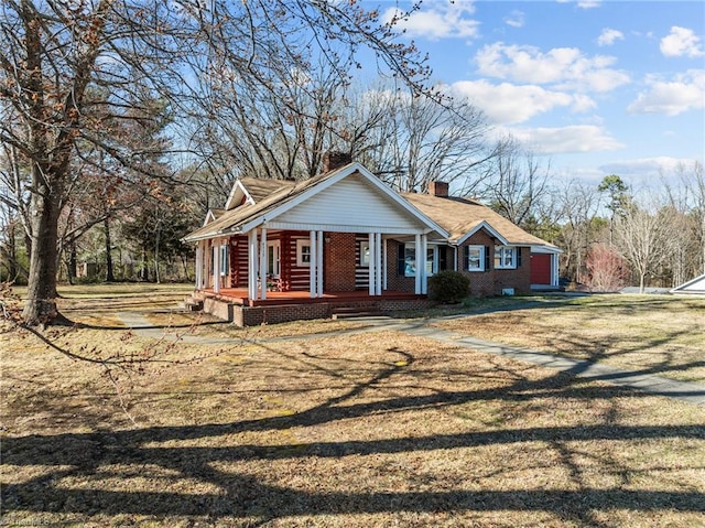 view of front of home with covered porch, brick siding, a chimney, and a front yard