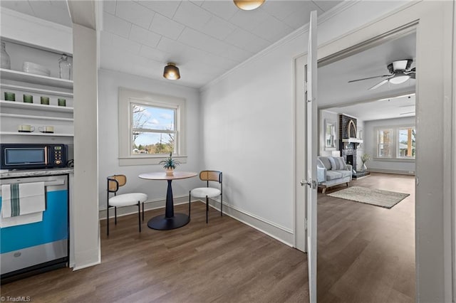 interior space with a large fireplace, baseboards, ceiling fan, ornamental molding, and wood finished floors