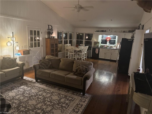 living room with dark wood-type flooring, ceiling fan, and vaulted ceiling