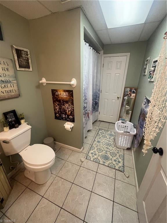 bathroom with a drop ceiling, tile patterned floors, and toilet