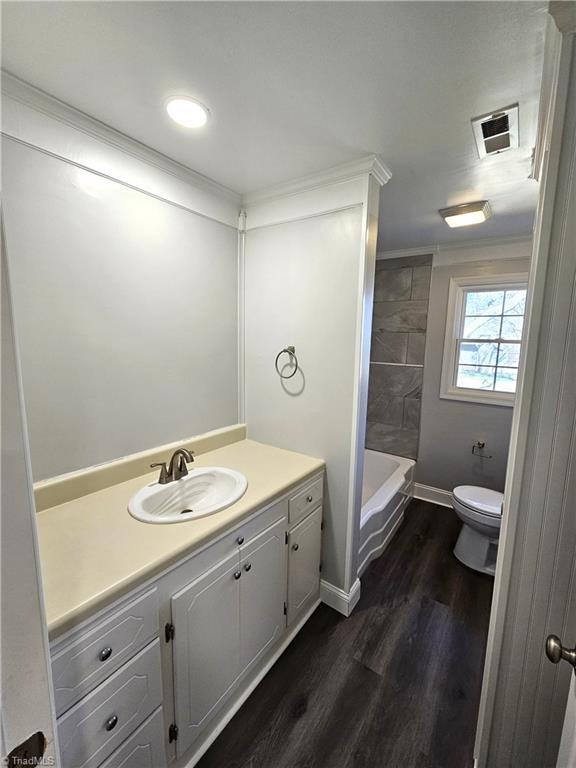 full bath featuring vanity, wood finished floors, visible vents, ornamental molding, and toilet