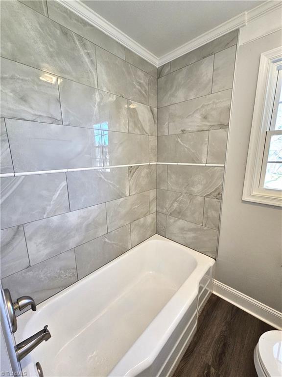 full bathroom with wood finished floors, baseboards, bathtub / shower combination, crown molding, and toilet