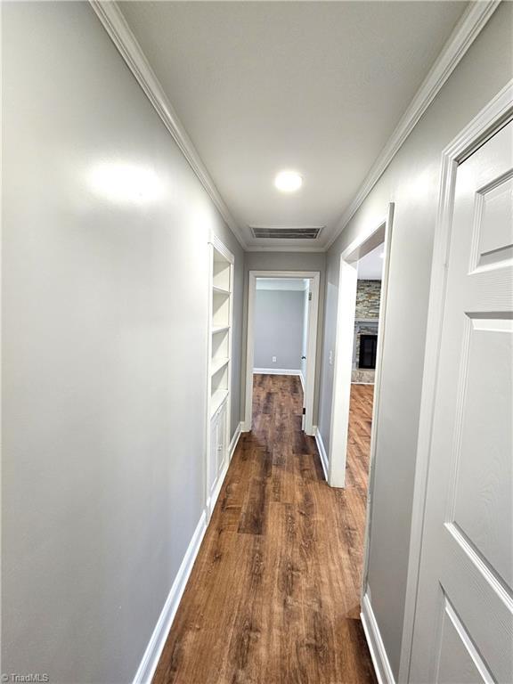 corridor featuring dark wood-style floors, built in shelves, baseboards, and ornamental molding