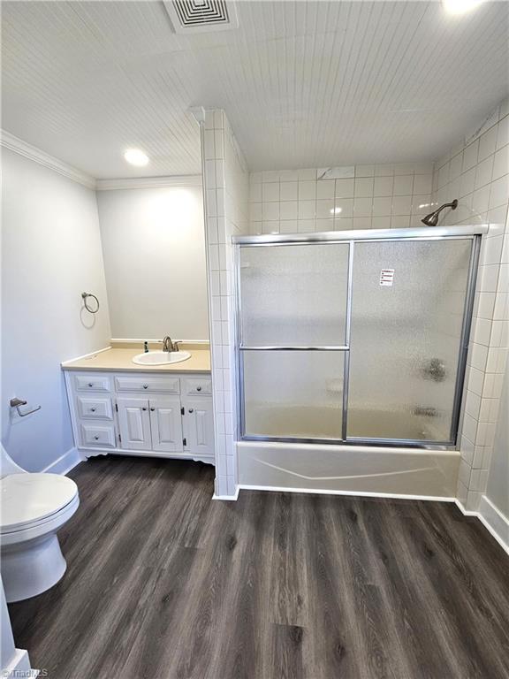 bathroom with vanity, wood finished floors, visible vents, bath / shower combo with glass door, and toilet