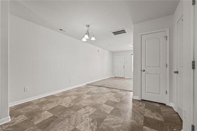 spare room with stone finish floor, baseboards, visible vents, and a chandelier