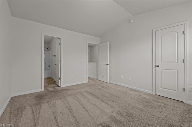 unfurnished bedroom with vaulted ceiling, carpet floors, ensuite bathroom, and baseboards