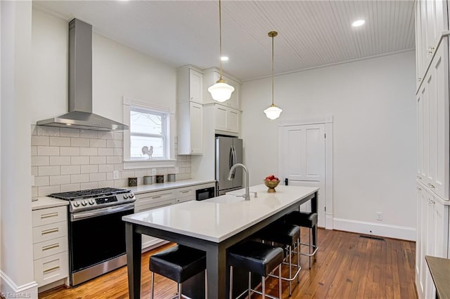 kitchen with a sink, tasteful backsplash, stainless steel appliances, a breakfast bar area, and wall chimney exhaust hood